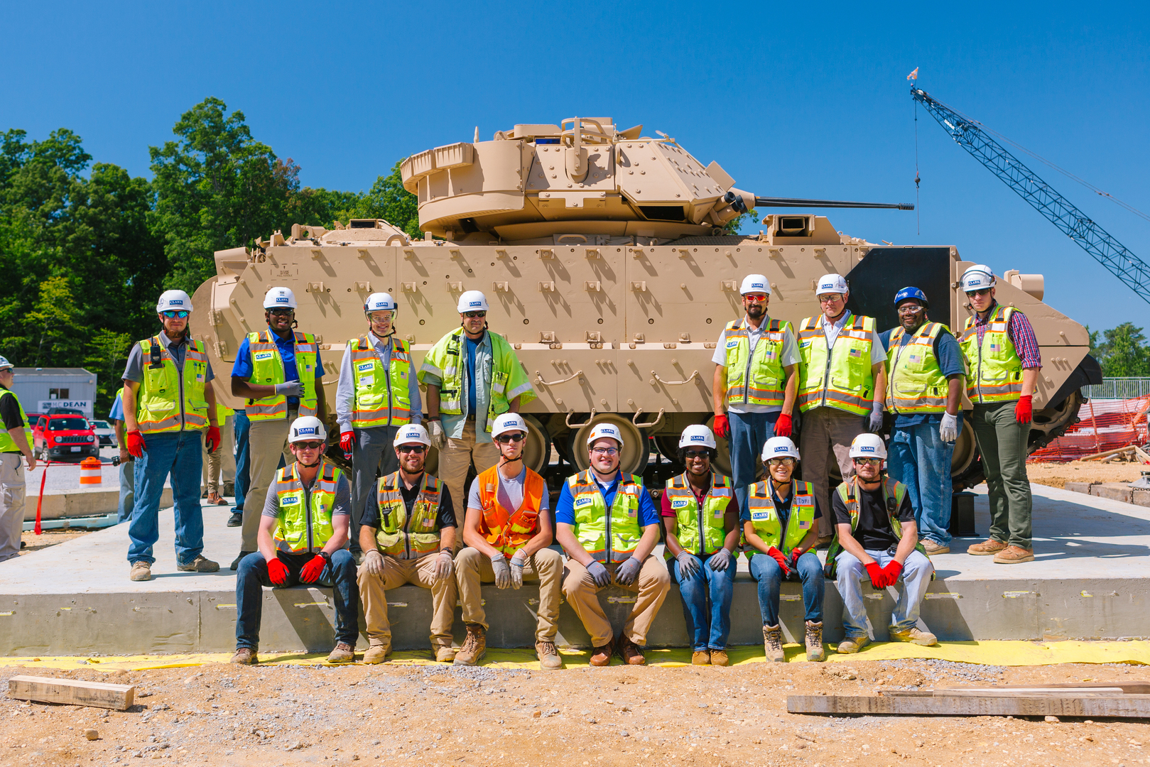 Clark employees in PPE pose in front of a sand-colored armored tank
