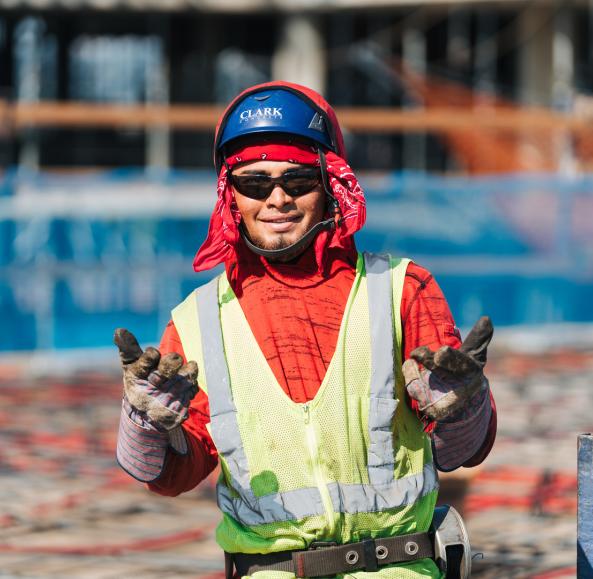Clark Concrete craft worker wearing PPE, red hoodie, and sunglasses smiles at camera