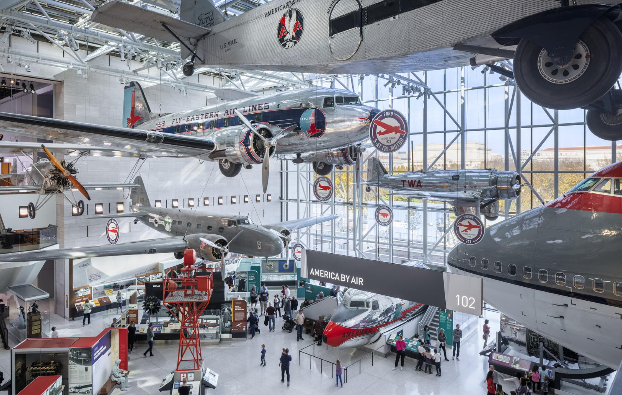 Silver airplanes are suspended in the air in an atrium of the Smithsonian's National Air and Space Museum